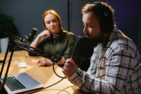 two radio hosts in headphones laughing while recording podcast in studio together.