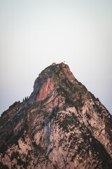 Vertical shot of a mountain peak and green trees at the slope at sunset