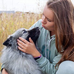 Young woman with her dog hugging and kissing in the field.