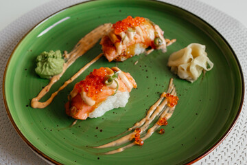 Sushi nigiri with a grilled salmon and caviar. Sushi rolls on green plate with wasabi and ginger. Top view with copy space. Traditional japanese dish.