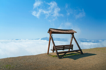 A wooden swing without people on the edge of a mountain over an abyss with a view of the clouds.