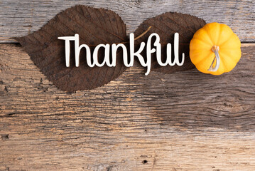 Simple, Thanksgiving background.  Thankful text with leaves and pumpkin, brown and orange on a rough wooden background.