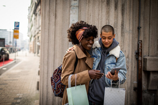 Lesbian couple with shopping bags using smartphone in city