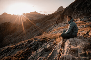Bergsteiger in Daunenjacke schaut in den Sonnenuntergang in den italienischen Bergen am Comer See, Bicacco Ledu - obrazy, fototapety, plakaty