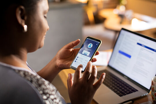 Back view woman checking bank account app on smartphone at home