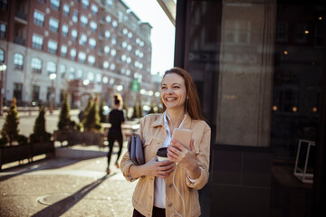 Smiling young woman with coffee cup using smartphone in the city