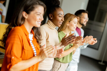 Young multiethnic startup team standing and applauding in the modern office