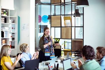 Young woman holding document getting applause from colleagues in office
