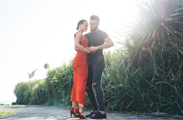 Stylish enamored multiracial couple dancing tango on path in tropical park