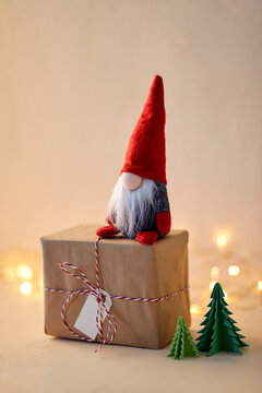 christmas, decoration and winter holidays concept - close up of gnome toy, gift box and fir trees made of green paper on beige background