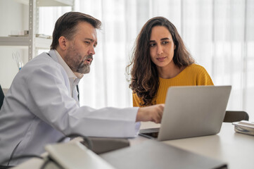 Male doctor talking to woman about illness in clinic. Caucasian doctor to check up health female in examination hospital room. Healthcare and medical concept.