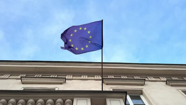 EU Flag on a building, European Union Flag waving in the wind against the blue sky. Zoom in effect.
