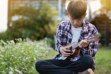 Asian cute boy playing acoustic guitar and ukulele in the backyard of his house.