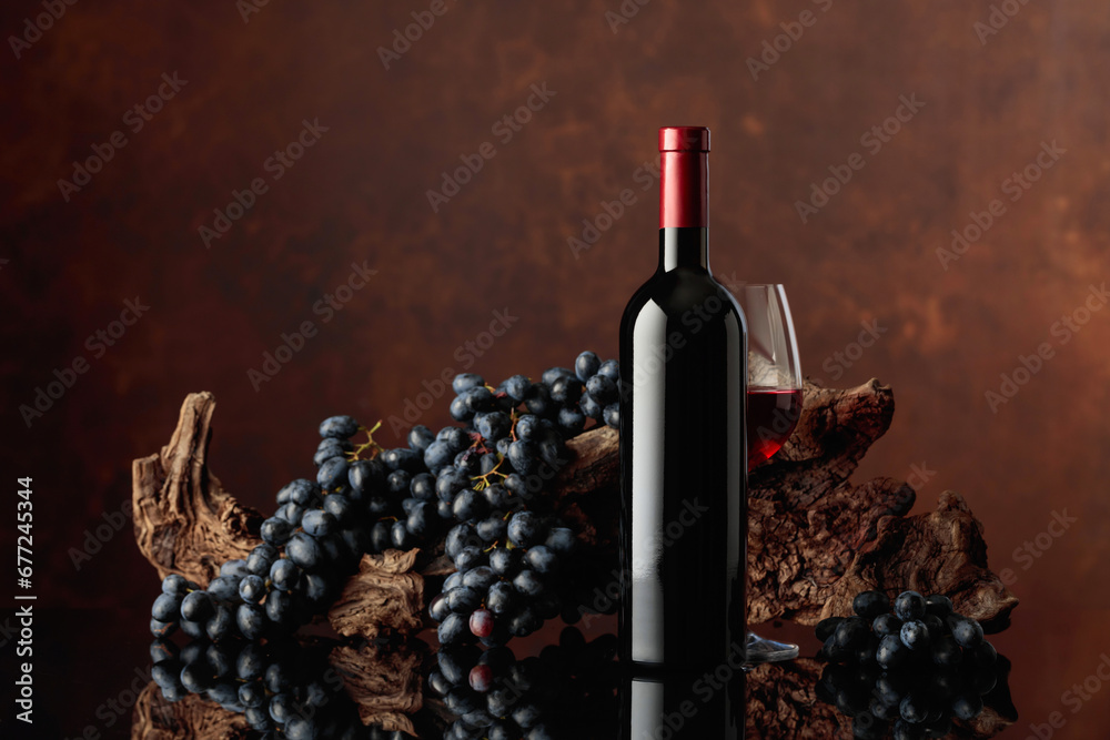 Poster Bottle and glass of red wine with an old snag and blue grapes.