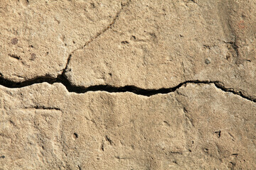 Crack in the concrete cladding of an old house. Rough, uneven surface. Cement plaster on a brick wall, texture, background. Ancient backdrop of yellowed color. Yellow, faded view of the wall cladding