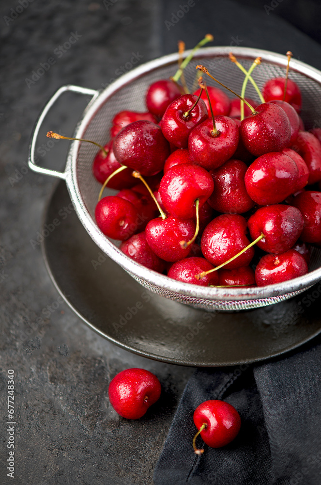 Sticker Seasonal harvesting of berries and fruits for the winter. Cherry jam. Cherry summer background. A large number of cherries with leaves on the table in a saucepan on a black background. close-up.