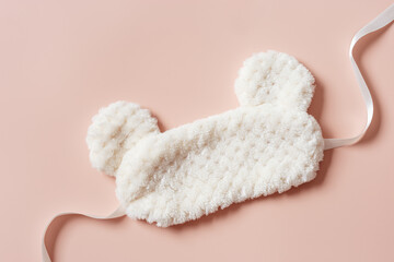 Sleeping mask from light fur on pale pink background. Still life details, cozy life style photo. Fluffy eye mask for best sleeps. Concept of home comfort and wellbeing, health sleep, minimal
