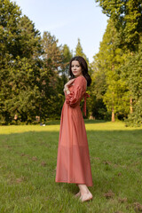 Naklejka premium Profile portrait of a beautiful brunette girl in dress posing in the park, green tree background. 