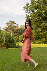 Portrait of a seductive brunette girl in dress posing in the park, tree background.
