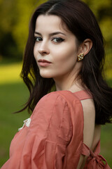 Portrait of a beautiful brunette girl in dress posing in the park, looking at the park.
