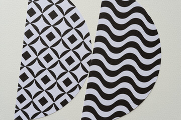 two machine-cut paper shapes with diamond in square and wavy line patterns on blank paper
