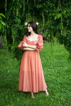 Image of a beautiful brunette female model in dress posing in the park, tree background.
