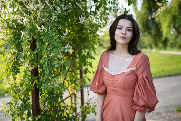 Portrait of a beautiful brunette girl in dress posing in the park, tree background.
