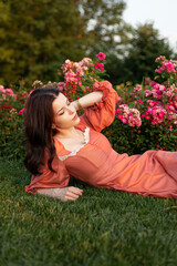 Profile portrait of a beautiful brunette girl in dress posing in the park, flowers background.
