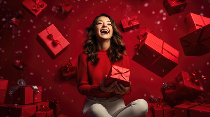 A joyful woman with curly hair, laughing and holding a red gift with a ribbon, surrounded by more festively wrapped presents, all against a vibrant red background.