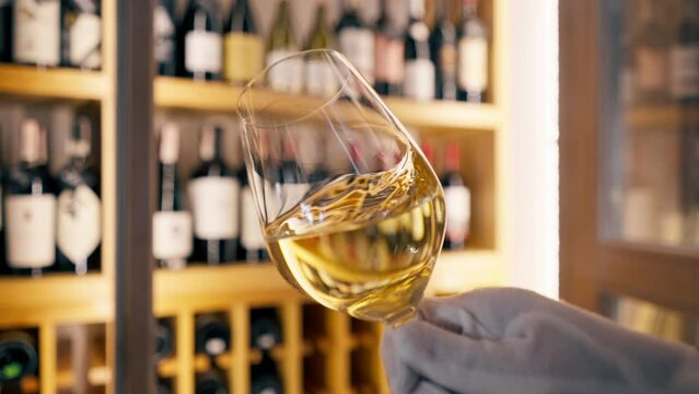 A close-up of a wine glass held by a sommelier in an Italian restaurant against the background of a wine shelf
