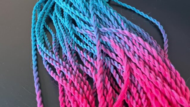 Colored braids with bright pink and blue elastic bands on a black background closeup