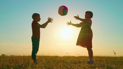 Children play with big ball in park against backdrop of sun. Happy child throws ball with his hands. Kids, boy, girl have fun with ball in park at sunset. Sports games for children outdoors. Family - obrazy, fototapety, plakaty