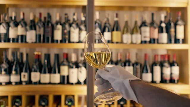 A close-up of a wine glass held by a sommelier in an Italian restaurant against the background of a wine shelf