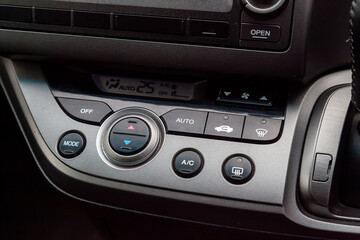 Close-up of the center console on a gray panel inside the car, with climate control and a red emergency button. Setting up and refueling the air conditioner in the workshop.