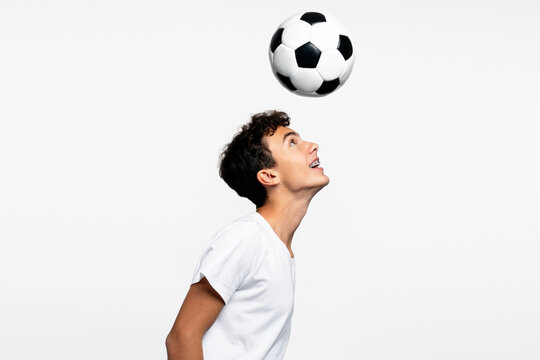 Smiling handsome teenage boy playing soccer, kicking ball with his head isolated on white background