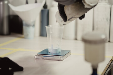 Woman in black protective gloves filling gun with paint in car workshop. Master adds paint to airbrush before before the spraying procedure.