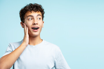 Handsome smiling teenage boy looking away isolated on blue background, copy space