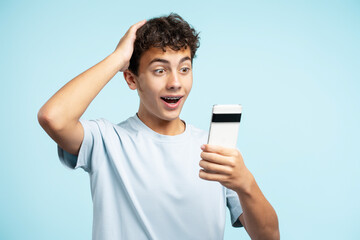 Excited attractive guy holding mobile phone isolated on blue background. Advertisement concept