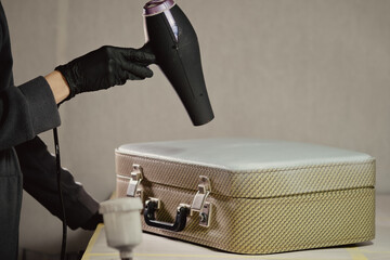 The workplace of the master restorer. Repair of leather goods. Blow-drying of the repair part on a leather suitcase. A hair dryer in women's hands.