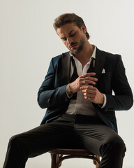 cool elegant man in tux with open collar shirt looking down and fixing rings