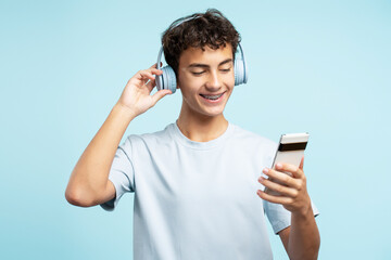 Portrait of smiling handsome teenage boy wearing headphones, holding mobile phone listening to music