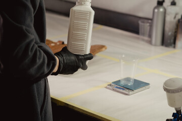 A woman in black protective gloves takes a white bottle with a primer in the workshop. Unscrews the...