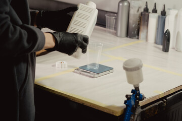 Woman in black protective gloves filling plastic bowl with paint in car workshop. Master adds primer to plastic bowl before before the spraying procedure.