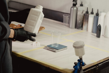 Woman in black protective gloves filling plastic bowl with paint in car workshop. Master adds primer to plastic bowl before before the spraying procedure.