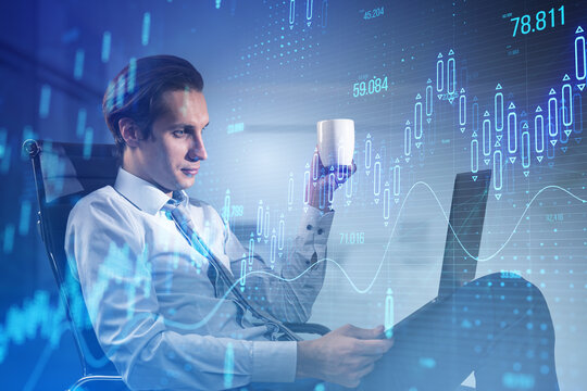 Attractive young businessman sitting and using laptop with glowing candlestick forex chart on blurry office interior background. Stock market and investment concept. Toned image. Double exposure.