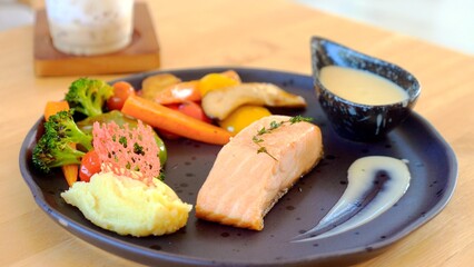 Gourmet salmon steak with roasted potatoes and grilled vegetables, served on a wooden table. Healthy and delicious meal for lunch or dinner.