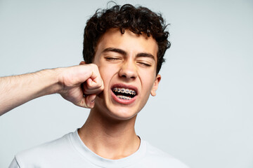 Portrait of upset attractive boy with braces with closed eyes, fist hitting face