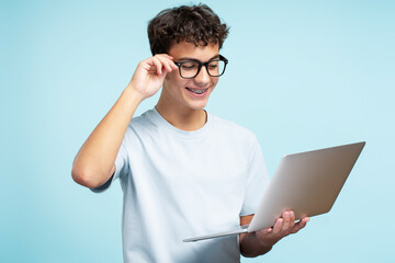 Portrait of handsome teenage boy wearing eyeglasses, holding laptop, using website