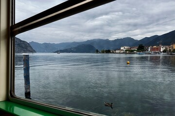 Vista del lago attraverso il finestrino di una nave traghetto con lo sfondo di montagne - obrazy, fototapety, plakaty