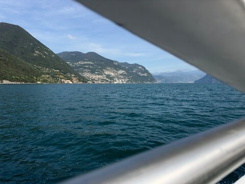 Vista del lago attraverso un parapetto di una nave traghetto con lo sfondo di montagne